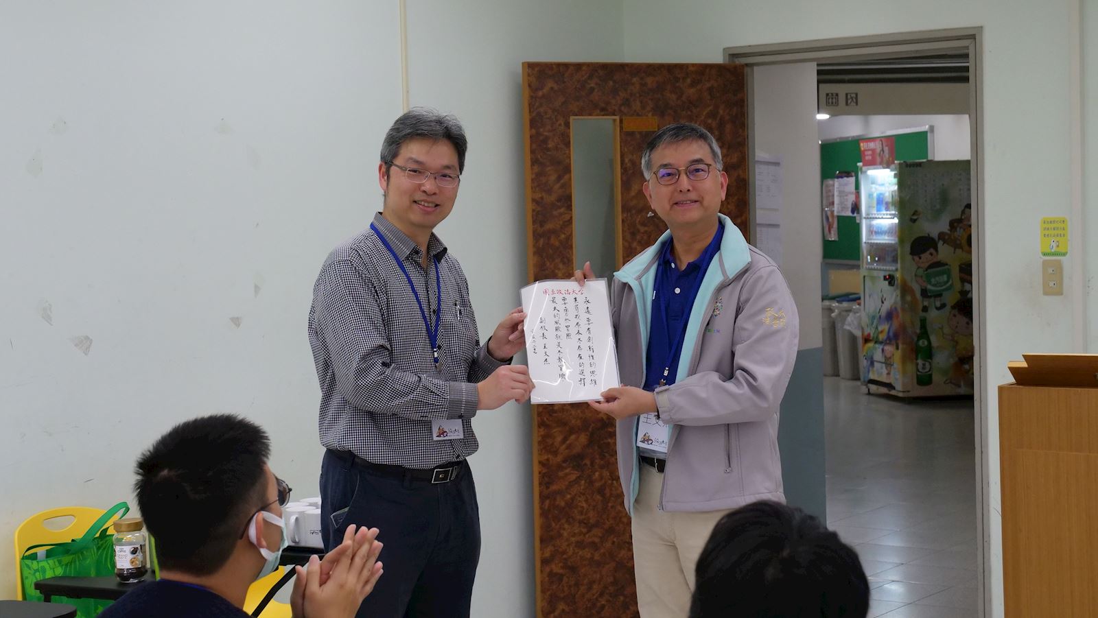 USR共好文山計畫主持人、副校長王文杰（右）親自題字給予學生助理勉勵，並將字簽交與USR共好文山計畫執行長、經濟系副教授王信實（左）